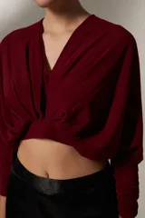 Blusa cropped de color negro, con cuello en V, mangas largas con puños ajustados y detalle de frunces en el frente.