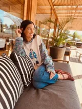 Sweater tejido con cuerpo en color crudo y mangas en lana multicolor. Presenta un diseño frontal estampado estilo vintage y detalles de tejido a crochet en cuello y puños.