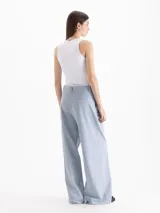 Pantalón de vestir tiro alto color celeste, de corte wide leg y largo hasta el suelo, con bolsillos delanteros decorados con volados tableados y bolsillos ojal en la espalda.