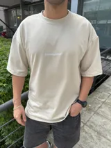 Remera de corte oversize en color beige, confeccionada en algodón pesado. Presenta cuello redondo acanalado y un pequeño bordado con el logo de la marca en el centro del pecho.