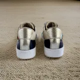 Championes de cuero con cierre de velcro, en combinación de colores blanco, negro y dorado texturizado, con detalles de arte pintado a mano en tonos turquesa y tostado en los laterales.