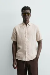 Camisa de lino color beige de corte relajado, con cuello solapa, manga corta y cierre frontal con botones.