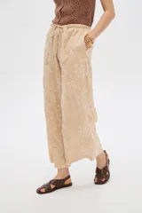 Pantalón ancho de poliéster color beige con diseño bordado floral en hilo blanco, cintura elastizada con cordón ajustable.