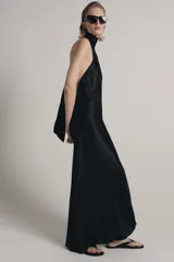 Vestido largo de satén negro con cuello halter subido y espalda descubierta. Presenta un diseño fluido con bajo en línea evasé.