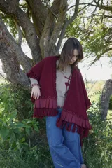 Ruana de tejido con textura en color bordó, con diseño amplio y fluido. Presenta detalles de volados aplicados en el cuello y ruedo, terminaciones con flecos y lazo frontal regulable.
