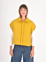 Chaleco puffer corto de color gris, con cuello camisero y cierre frontal oculto. Presenta un diseño holgado y sin mangas.