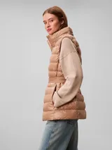 Chaleco puffer acolchado color tostado de la marca Calvin Klein, con diseño sin mangas, cuello alto y capucha desmontable. Cuenta con cierre frontal de cremallera y un cinturón elástico ajustable con hebilla de clip con el logo de la marca.
