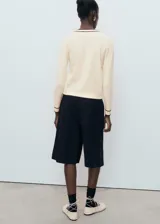 Jersey de punto fino en color crema con cuello de pico y detalles en contraste color marrón en el cuello y los puños. Presenta un diseño recto de manga larga.