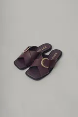 Sandalia plana de cuero color borgoña, con tira ancha cruzada sobre el empeine y hebilla metálica dorada. La suela es delgada y oscura.