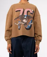 Buzo de algodón color marrón, con cuello redondo y mangas largas abullonadas con puños ajustados. Presenta un estampado grande con el número "76", un águila americana y texto. El borde inferior es cortado y deshilachado.