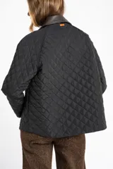 Campera negra de diseño capitoneado con cuello de solapa en contraste color marrón. Presenta cierre frontal con cremallera y botones a presión, mangas largas con puños ajustables y un corte recto.