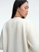 Sweater de tejido de punto acanalado en color blanco, con cuello redondo, mangas largas y corte holgado. Presenta un diseño minimalista y contemporáneo.