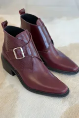 Botin de cuero color bordeaux con diseño de textura combinada, punta cuadrada y hebilla metálica lateral.