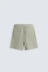 Bermuda negra de corte regular, confeccionada en tejido jacquard con efecto arrugado. Presenta cintura elástica ajustable con cordón blanco, bolsillos laterales y bolsillos traseros de vivo.