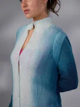 Saco largo de lana merino tejido con diseño jacquard de ramas, de líneas rectas y aberturas laterales, con efecto degradado en tonos azules y blancos, mangas largas con puños entallados y cierre frontal con pequeños botones.