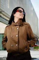 Campera de gamuza color marrón, con diseño de doble botonadura, cuello alto con tira y hebilla ajustable, y bolsillos laterales.