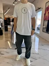 Remera blanca de manga corta con estampa en la espalda que incluye la frase 'Focus on finding joy in the journey' formando un círculo alrededor de la figura de un pájaro con sombrero.