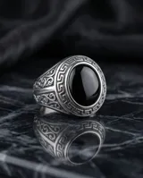 Anillo de acero tipo sello con piedra central redonda color negro y detalles de guarda griega en los laterales.