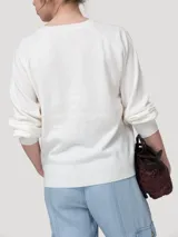 Sweater de punto color beige claro, con escote redondo y cierre frontal parcial de botones con reborde metalizado, mangas largas abullonadas y puños y ruedo elásticos.