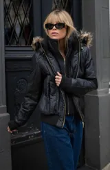 Campera negra de estilo urbano con diseño acolchado, cierre frontal dorado y cuello alto con textura. Incluye capucha con borde de piel sintética y puños de tejido acanalado.