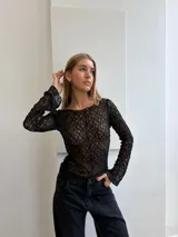 Top de encaje negro con diseño floral, de corte ajustado y manga larga.