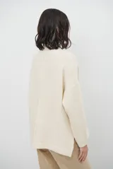 Polera de tejido de punto color chocolate, con cuello alto, mangas largas con puños acanalados y detalle de costura central vertical. Incluye una pequeña etiqueta de cuero sintético en el ruedo.