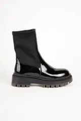 Botas negras de caña media, confeccionadas en símil cuero charol y tela elastizada. Presentan punta redonda y suela tipo tractor de 5 cm de alto.