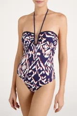 Malla enteriza de color azul marino con estampado geométrico abstracto en tonos blancos y anaranjados, escote en U pronunciado con detalles de bordado trenzado y tirantes halter con borlas colgantes.
