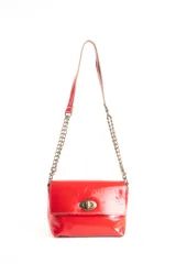 Cartera roja de charol con correa doble, una parte de cuero y otra de cadena metálica. Tiene cierre de broche metálico dorado.