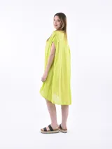 Vestido camisero de corte holgado y diseño asimétrico, con cuello clásico, cierre frontal de botones y mangas cortas con terminación caída.