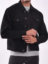 Campera de jean negra, estilo trucker, con cuello camisero, cierre frontal de botones y dos bolsillos superiores con tapa y botón.