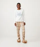 Pijama largo de dos piezas en tejido fleece. Incluye un buzo blanco de manga larga con bordado "Lazy Sunday Mood" en el frente y un pantalón largo con estampado de cuadros beige, negro y azul.