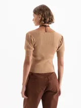 Top de punto acanalado color beige, con escote redondo amplio, mangas cortas abullonadas y cierre frontal mediante ganchos decorativos con piedras.
