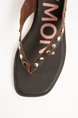 Sandalias planas de cuero marrón tipo ojota con tiras anchas adornadas con tachas metálicas plateadas y plantilla con diseño estampado.