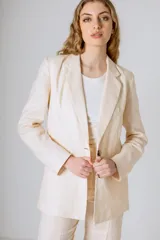 Blazer color beige confeccionado en lino, con solapas clásicas, cierre frontal de dos botones y bolsillos con solapa en los laterales.