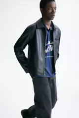 Campera de cuero sintético color negro con cuello camisero, cierre frontal, bolsillo superior con cierre y bolsillos laterales ribeteados.