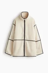 Campera de corte holgado confeccionada en tejido de sherpa suave, con cuello alto y cierre frontal. Presenta detalles de ribetes en contraste y diseño de hombros caídos.