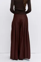 Pantalon de vestir color marron, de corte ancho y tiro alto, con diseño plisado y detalles de bolsillos frontales con botones.