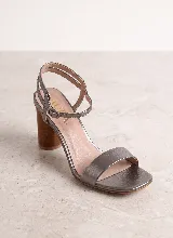 Sandalia de cuero color tostado, con taco alto ancho símil madera y tira ancha en la parte delantera. Presenta doble tira ajustable con hebilla en el tobillo.