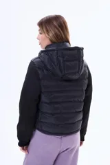 Campera negra de estilo híbrido, con cuerpo acolchado y mangas de tejido liso. Presenta cuello alto, cierre frontal y puños elásticos.