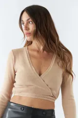 Top tejido de punto con diseño cruzado, escote en V y mangas largas. Cuenta con tiras para anudar en la cintura y detalle de grifa de cuero.