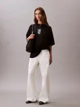 Remera de corte oversize confeccionada en algodón, con cuello redondo y mangas cortas. Presenta un estampado frontal con el logo de la marca en disposición vertical.