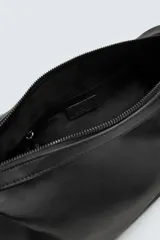Bolso tipo bandolera de diseño minimalista en color negro, con cierre de cremallera superior y asa de hombro ajustable. Incluye un detalle decorativo de charms metálicos en uno de los laterales.