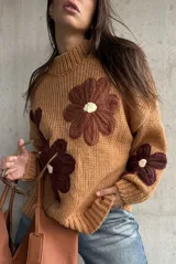 Sweater de punto grueso color camel, con diseño de flores grandes aplicadas en tonos marrones y centro crema. Presenta cuello redondo alto, mangas largas con hombros caídos y terminaciones acanaladas.