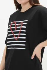 Remera de algodón negro con cuello redondo y diseño holgado, con estampado frontal de líneas horizontales blancas y un corazón rojo superpuesto.