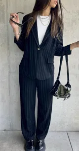 Blazer negro con finas rayas verticales blancas, solapas de muesca, cierre frontal con un botón y bolsillos laterales.