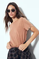 Remera de manga corta color marrón con escote a la base y calce relajado. Las mangas presentan terminación con ojales metálicos.