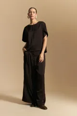 Top negro de manga corta con silueta amplia y caída fluida, confeccionado en un tejido liviano con leve brillo. Presenta un botón de nácar en la espalda con una pequeña abertura y mangas amplias tipo kimono.