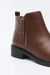 Bota corta de cuero sintético color negro, con taco bajo cuadrado y cierre lateral metálico. Presenta un detalle texturizado tipo reptil en la parte posterior del talón.