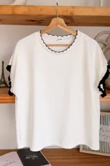 Remera negra de manga corta con detalles en contraste blanco en el cuello redondo y en los puños, con terminaciones onduladas.
